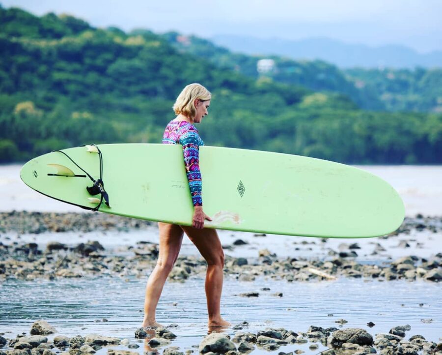 Female surfer carrying a green longboard into the water in Costa Rica.