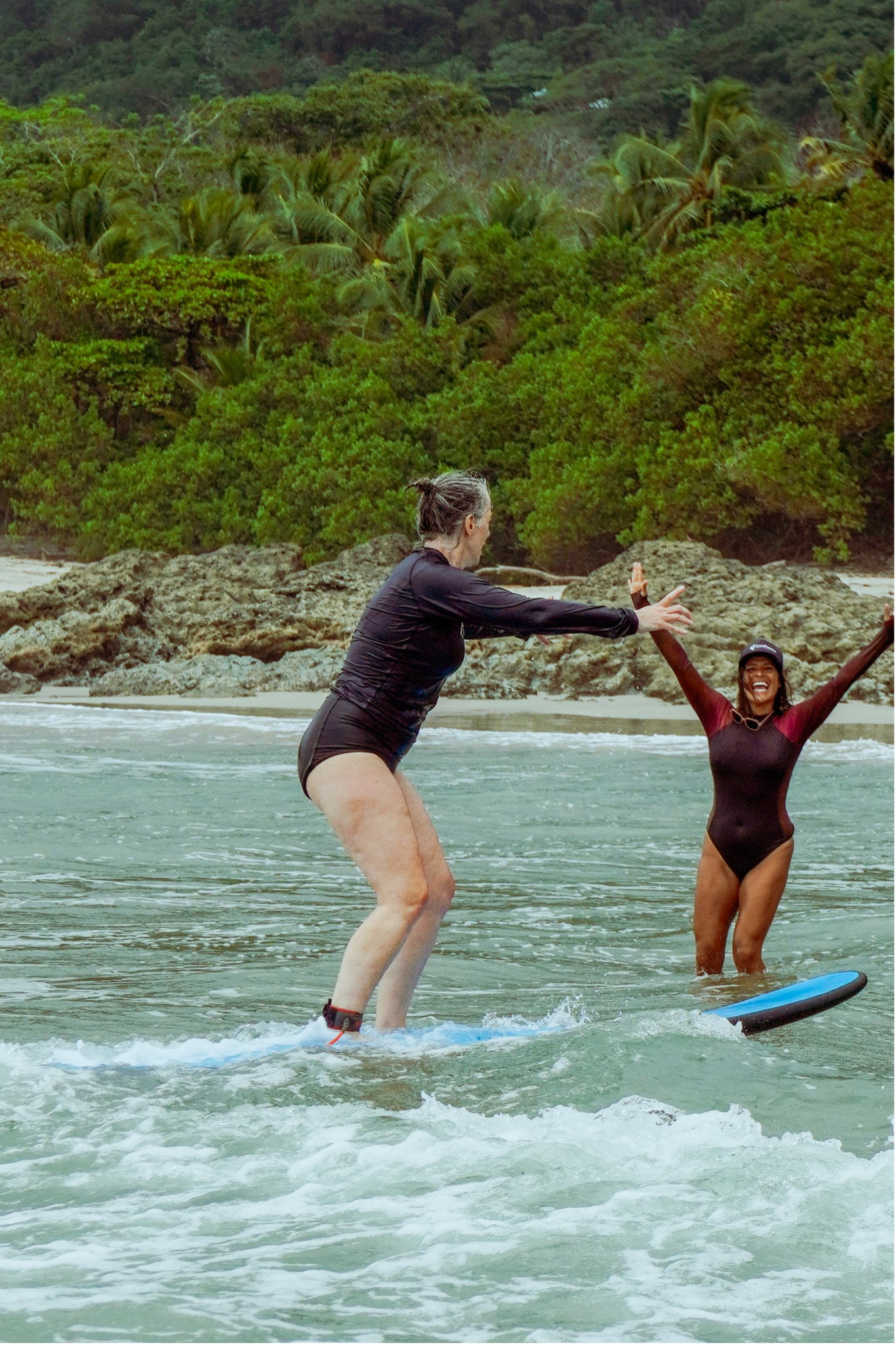 Smiling woman in her 50s riding a small wave at a women’s surf and yoga retreat in Santa Teresa, Costa Rica.