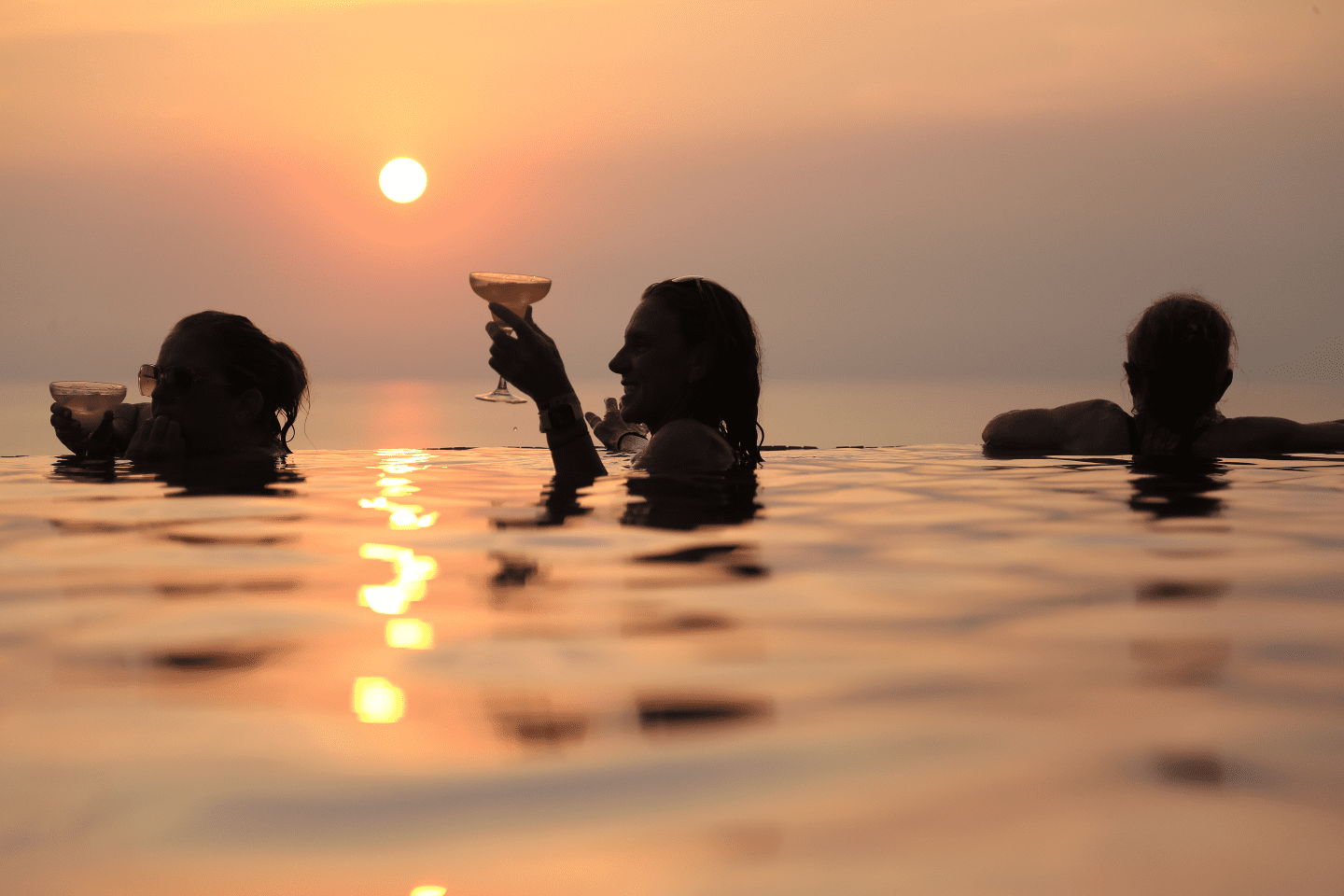 Women relaxing in an infinity pool at sunset with cocktails during a Costa Rica surf retreat