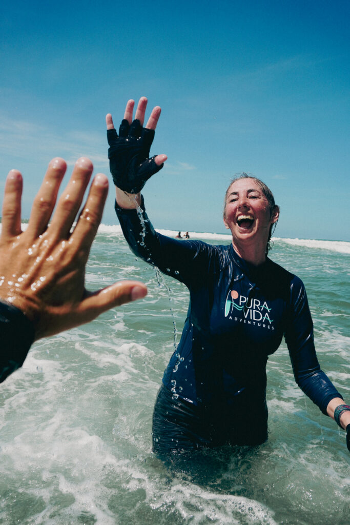 Pura Vida Adventures guest celebrating in the ocean after surfing at the Women 50+ retreat in Costa Rica