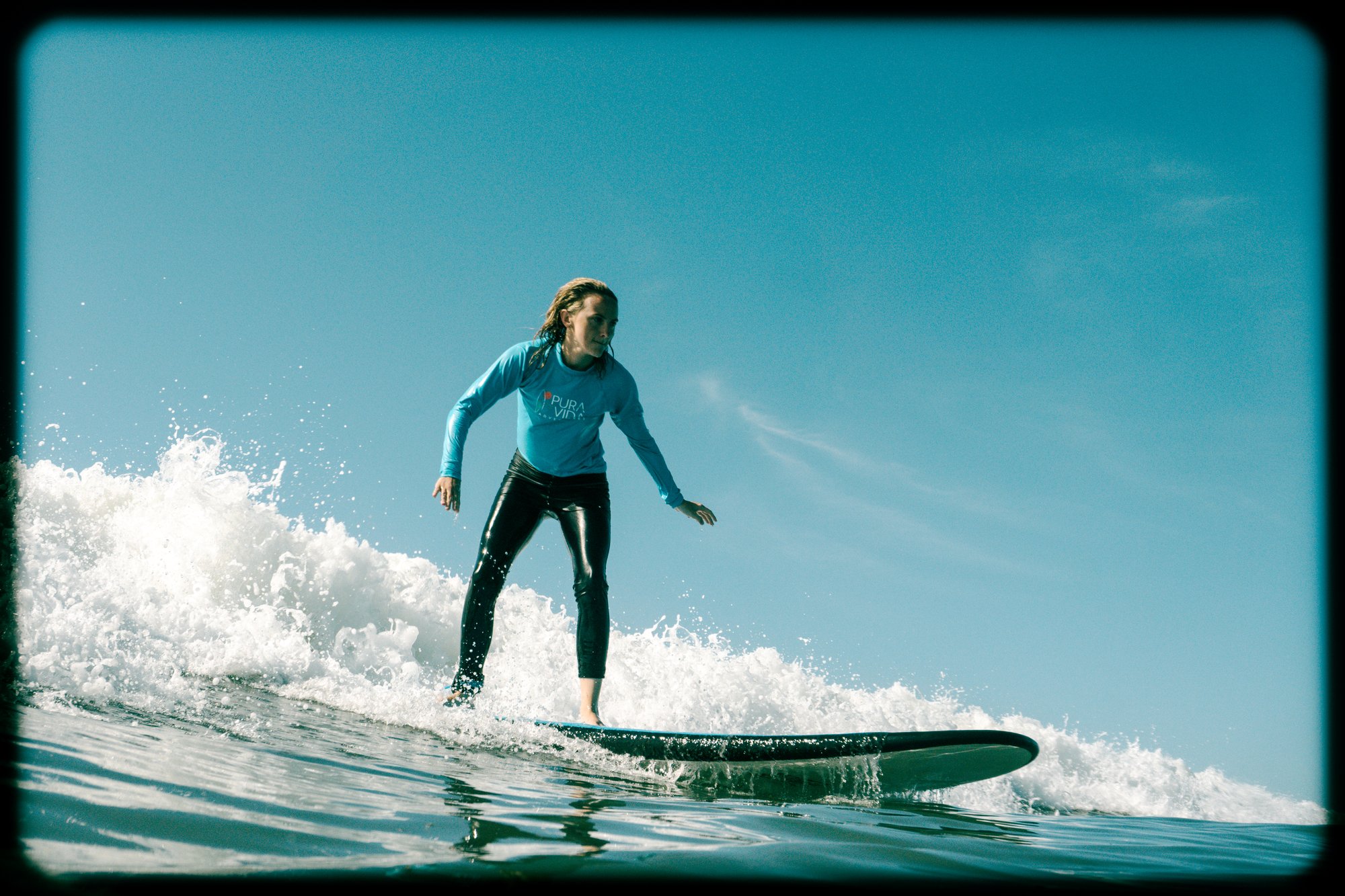 Woman standing on her surfboard riding a wave at a Pura Vida Adventures surf retreat in Santa Teresa, Costa Rica