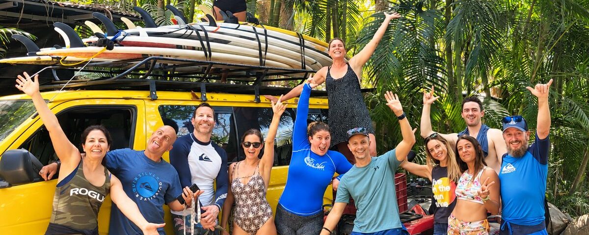 Pura Vida Adventures coed surf retreat group beside a vehicle loaded with surfboards in Costa Rica.